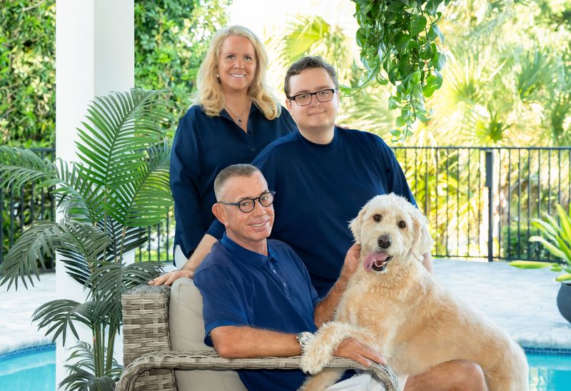 a family of three sitting in their backyard by a pool with their dog